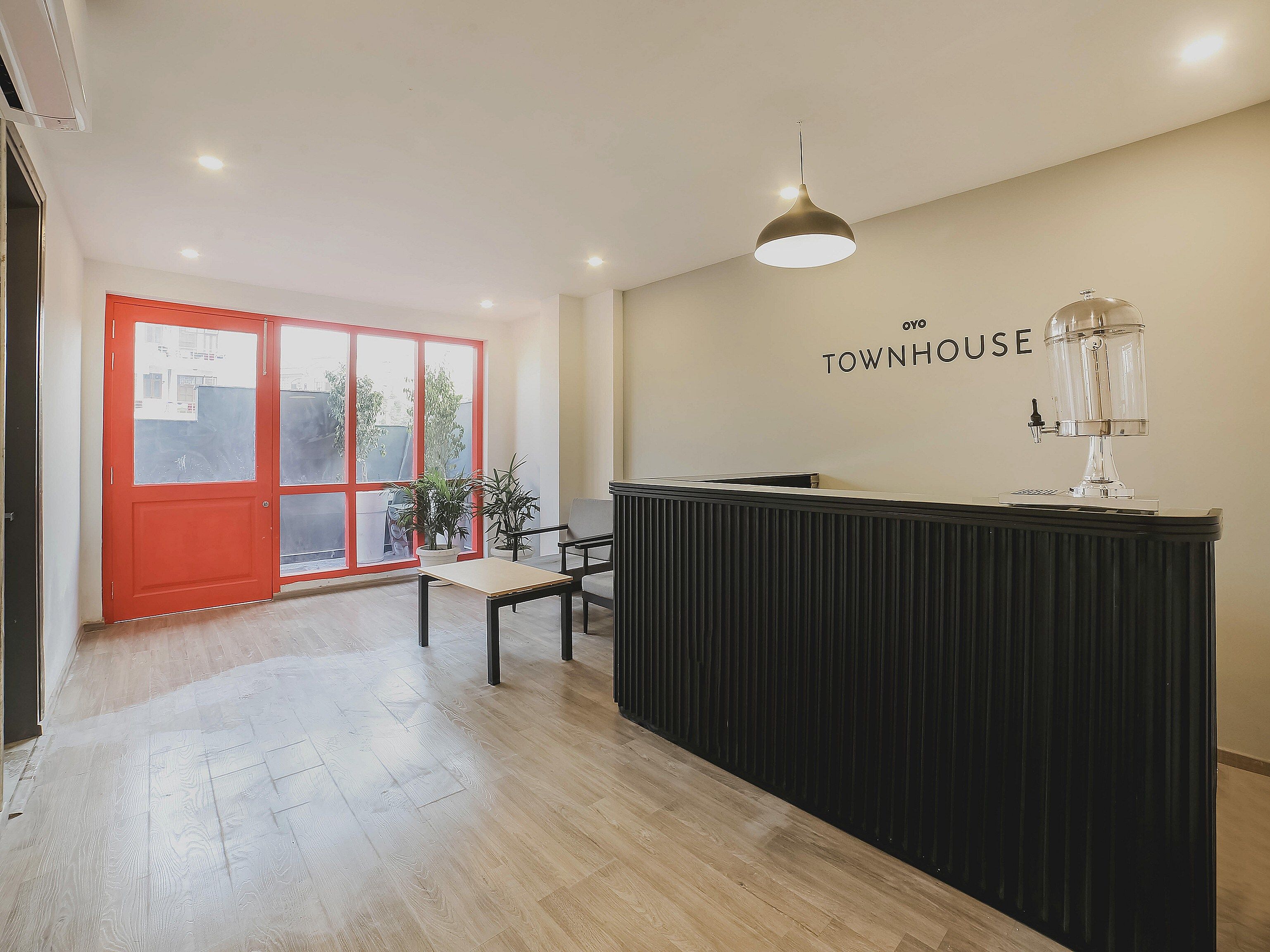 En receptionsdisk med en modern hänglampa, en röd dörr och en väggmonterad skylt med texten ”TOWNHOUSE”.