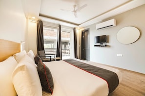 A hotel room with a bed, a TV, an air conditioning unit, a balcony with a chair, and a view of a brick building. - Townhouse Sector 46 Gurgaon Near (Gurugram)