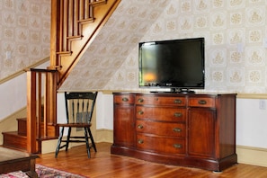Una escalera con barandillas de madera, una silla de madera, un armario con cajones y un televisor encima.