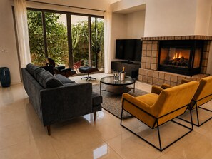 Ein modernes Wohnzimmer mit einer Couch, einem Couchtisch, Sesseln, einem Kamin und einem Fernseher.