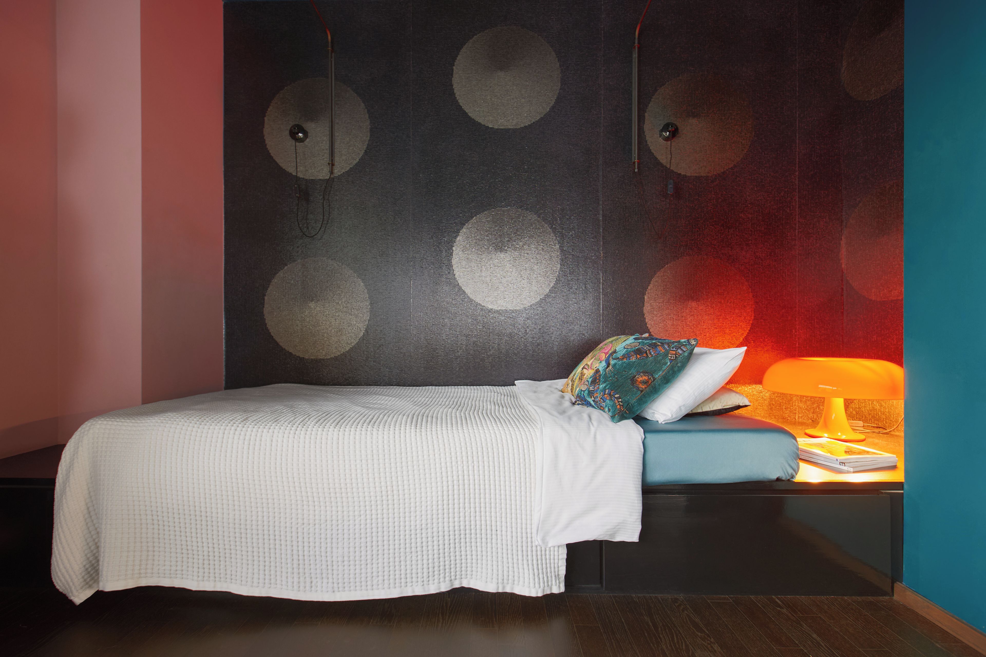 Ein Schlafzimmer mit einem Bett, einem Nachttisch, einer Lampe und einer Wand mit kreisförmigen Mustern.