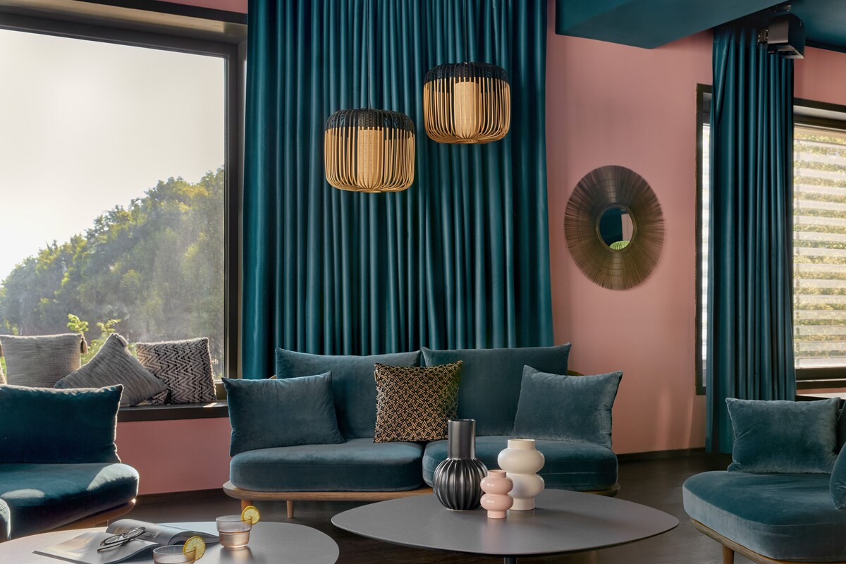 Un salon moderne avec un canapé, deux tables d’appoint et une grande fenêtre avec des rideaux.