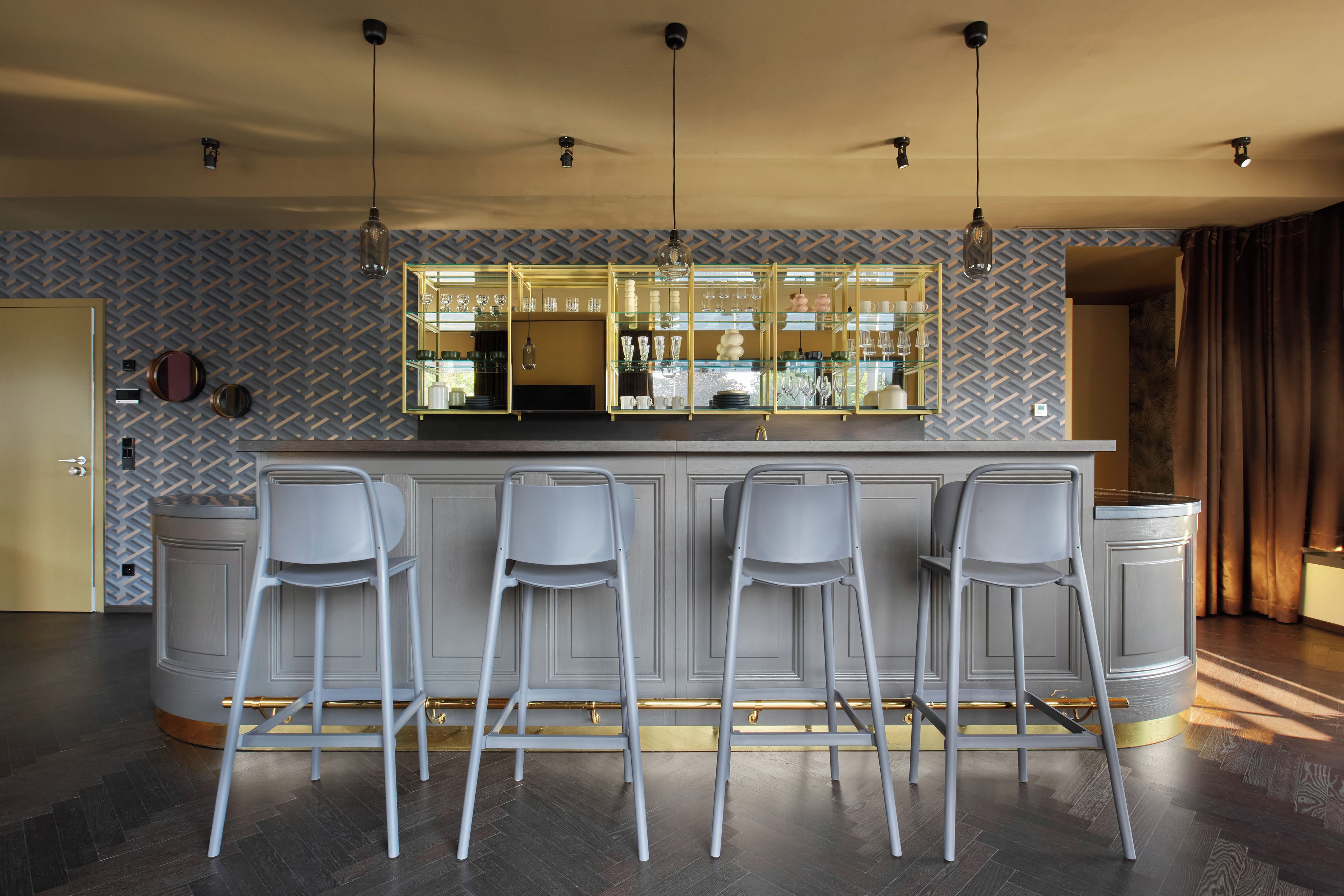 Un espace bar doté d’un mur arrière recouvert de miroirs, de tabourets de bar et de luminaires suspendus.