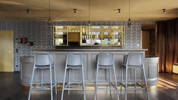 Un espace bar doté d’un mur arrière recouvert de miroirs, de tabourets de bar et de luminaires suspendus.