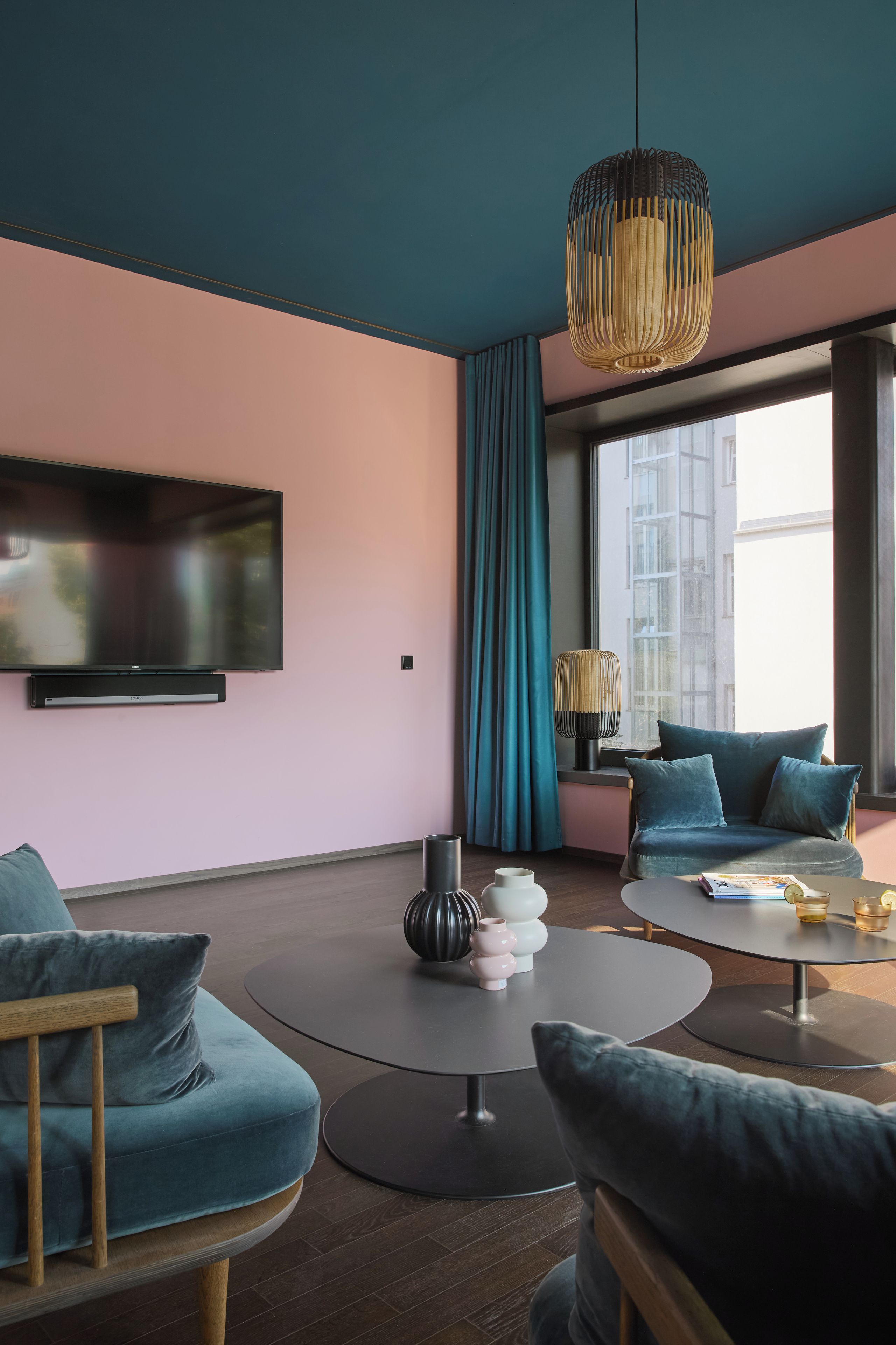 Un salon moderne doté d’un téléviseur à écran plat, de canapés de couleur turquoise, d’une table basse ronde et d’une grande fenêtre avec des rideaux.