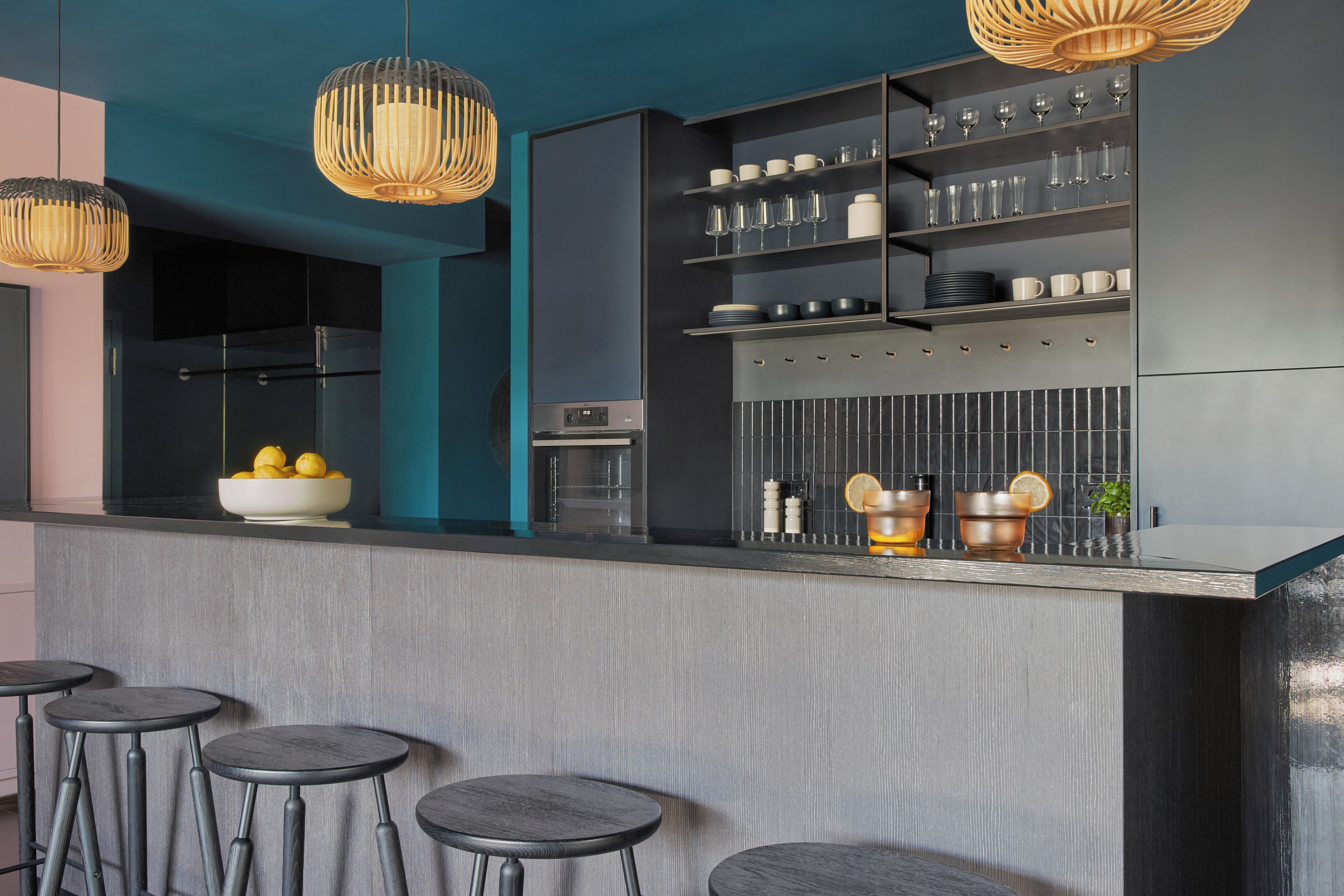 A modern kitchen with a bar area, featuring a built-in oven, a wine rack, and a bowl of lemons on the counter.