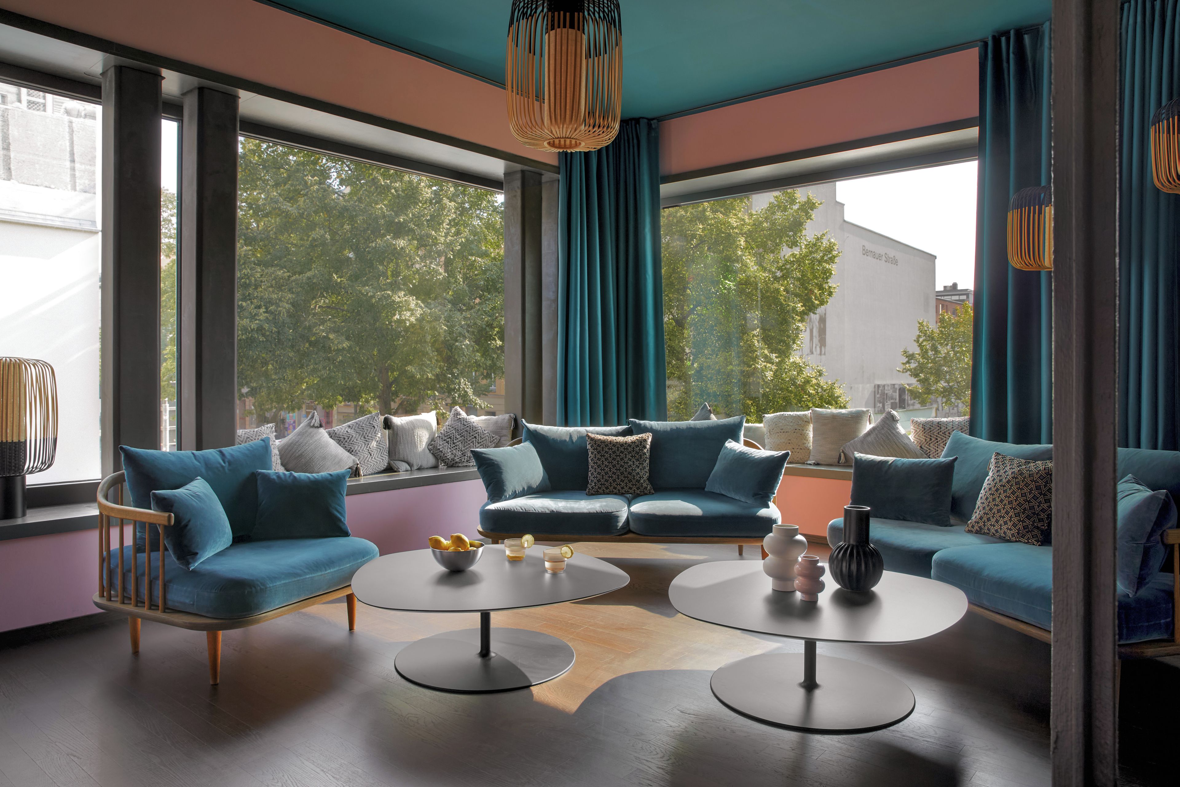 Ein modernes Wohnzimmer mit einer Eckcouch, zwei runden Tischen und großen Fenstern mit Vorhängen.