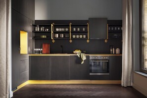 Une cuisine moderne avec des meubles de couleur sombre, un four encastré et une fenêtre avec des rideaux.