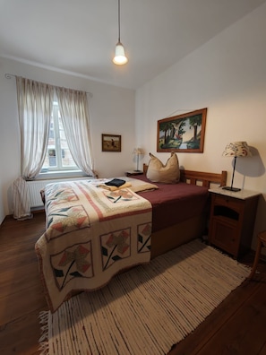 Una camera da letto con un letto, una finestra con tende, un quadro appeso al muro e una lampada da comodino.