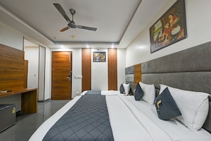 Habitación de hotel con cama, escritorio, armario, ventilador de techo y un cuadro en la pared.