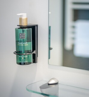 Een zeepdispenser op een glazen wandplank in een badkamer.