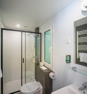 Een moderne badkamer met een douchecabine van glas, een toilet, een wastafel en een handdoekrek.