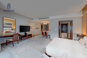 Ein Hotelzimmer mit einem großen Bett, einem Schreibtisch mit Stuhl, einem Fernseher und einem durchgegangenen Tür angedeuteten Badezimmer.
