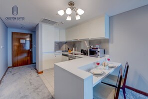 A modern kitchen with a central island, a microwave, and a dining area set up with a table and chairs. - Burj View Studio w/ Balcony | Dubai Mall Access (Dubai)