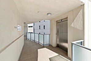 A corridor with a glass railing, an elevator, and a sign indicating apartment numbers. - Cityside Comfort – West Perth – 2BR with Pool & City Views (West Perth)