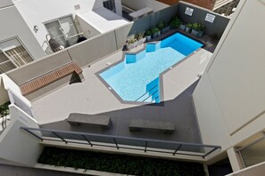 A rooftop pool with a clear blue water feature, surrounded by potted plants and a wooden bench. - Cityside Comfort – West Perth – 2BR with Pool & City Views (West Perth)