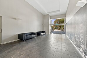 A spacious lobby with a black leather sofa, a glass partition, and a cityscape mural on the wall. - Cityside Comfort – West Perth – 2BR with Pool & City Views (West Perth)
