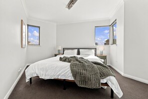 A bedroom with a bed, two bedside tables, a window, and a door. - Cityside Comfort – West Perth – 2BR with Pool & City Views (West Perth)
