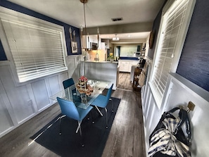 Dining area with a glass table and blue chairs, open to the kitchen — great for family meals. - Tipsy Tangerine Cottage | 2BR Near Madeira Beach (St. Petersburg)