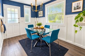 A dining area with a glass table surrounded by four chairs, a chandelier, and a potted plant.