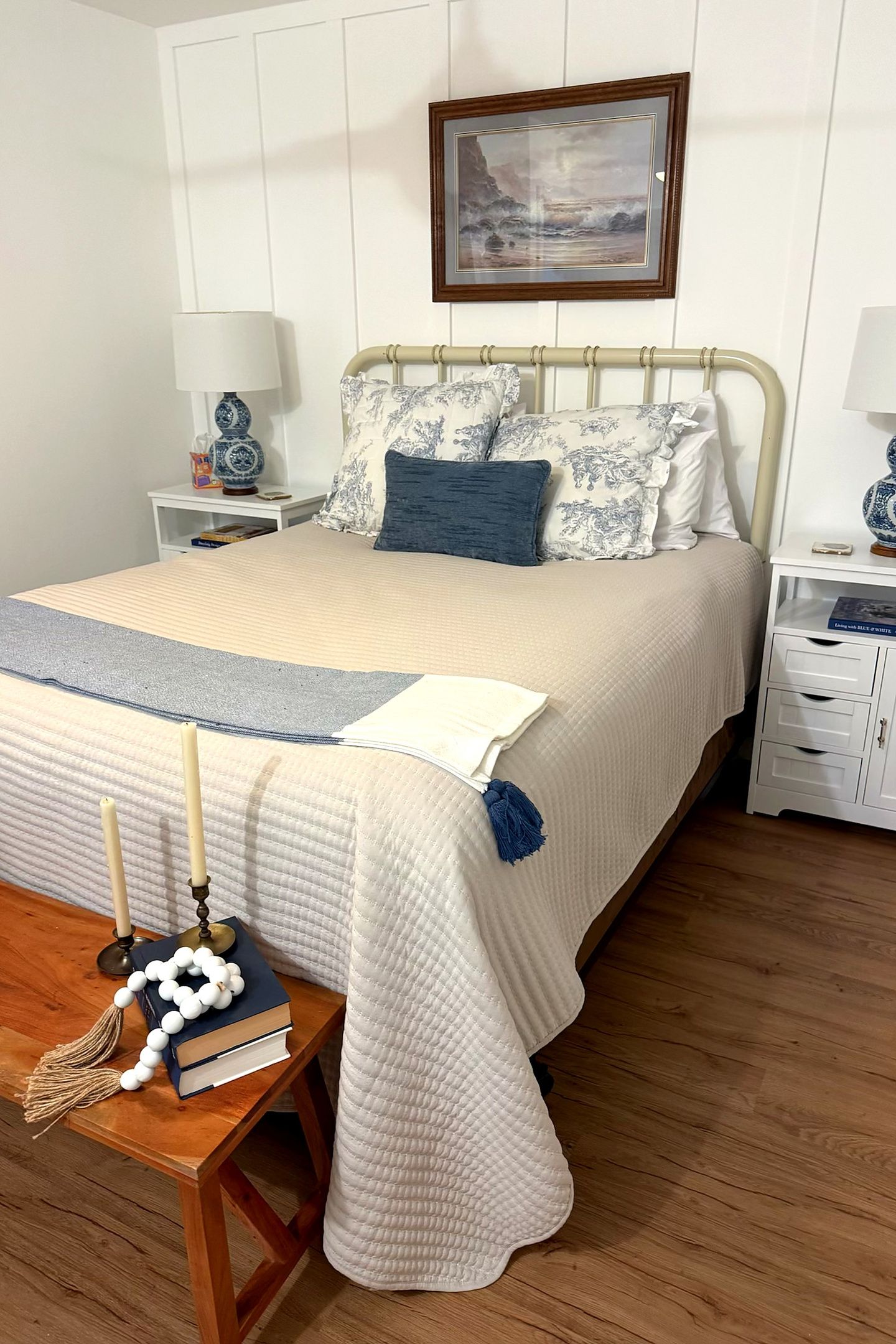 A neatly made bed with a quilted cover, a bedside table with a lamp, and a framed picture on the wall.