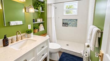 A bathroom with a white sink, a toilet, a shower with a glass door, and a window.