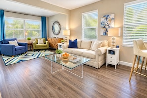 A modern living room with a glass coffee table, two sofas, a wooden cabinet, and a dining area with a chair.