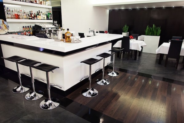 Zona de bar moderna amb un taulell blanc, tamborets i diverses ampolles de licors.