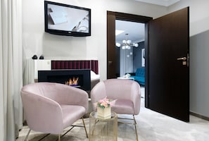 Una sala moderna con chimenea, dos sillones, un televisor y una puerta que da a otra habitación.