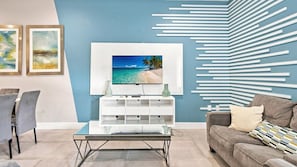 Un salon moderne avec un téléviseur à écran plat, une table basse en verre, un canapé et un meuble de rangement blanc pour les appareils électroniques.