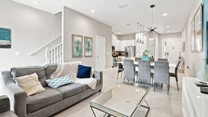A modern living room with a sofa, coffee table, and dining area with chairs. - Summerville Resort Prime Location Near Disney (Kissimmee)