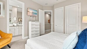 Une chambre à coucher comprenant un lit, une commode, un téléviseur et une salle de bain avec un lavabo et un miroir.