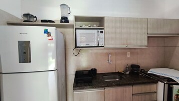 Cocina compacta con refrigerador, microondas y cafetera sobre la encimera.