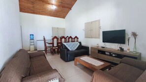 Ein Wohnzimmer mit einer Sofagarnitur, einem Couchtisch, einem Fernseher und einem Essbereich mit Stühlen und einem Tisch.