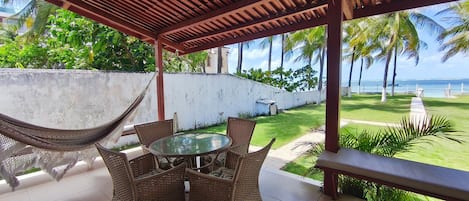 Patio esterno con tavolo rotondo e sedie in vimini, affacciato su un prato e vista sull'oceano.