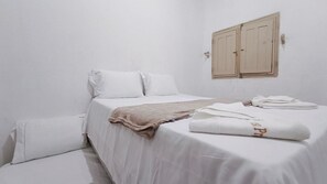 Ein Einzelbett mit weißer Bettwäsche, einer beigefarbenen Decke und einem gefalteten Handtuch.