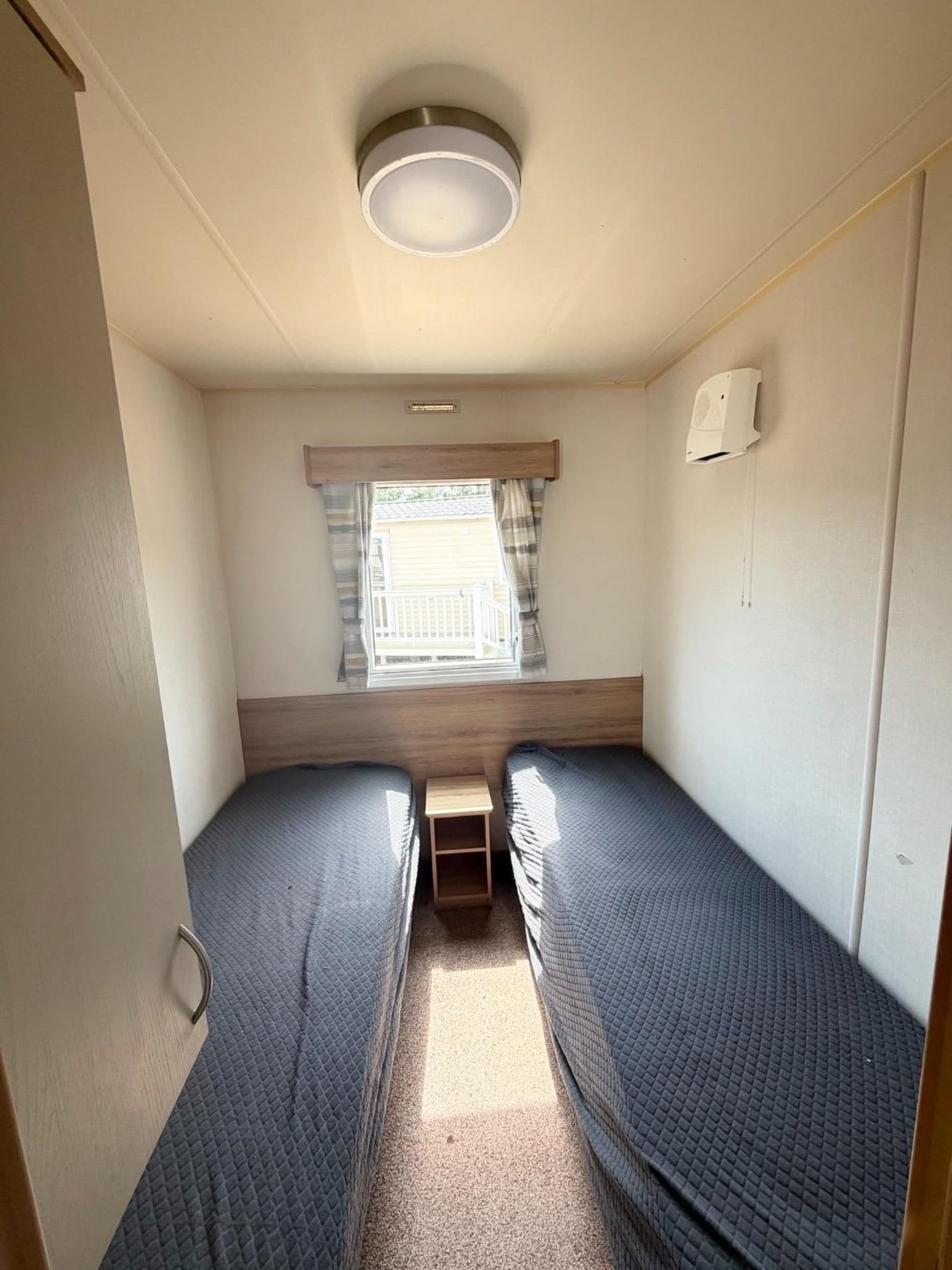 Interior compacto de autocaravana con dos camas, una ventana pequeña con cortinas y una lámpara en el techo.