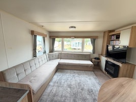 Interior compacto de uma motorhome com sofá, televisão e pequena cozinha.