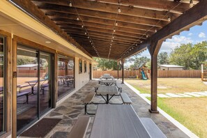 A covered patio area with stone flooring and picnic tables. - Guadalupe Bluff Trail House - Guadlupe Rivew View - Playset - (Kerrville)