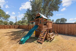 A wooden play structure with a slide and climbing steps. - Guadalupe Bluff Trail House - Guadlupe Rivew View - Playset - (Kerrville)