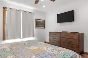A bedroom with a bed, a dresser, a television, and a window with curtains. - Guadalupe Bluff Trail House - Guadlupe Rivew View - Playset - (Kerrville)