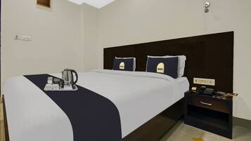 Una habitación de hotel con cama, una mesita de noche con teléfono, una bandeja con tetera y un interruptor de luz en la pared.