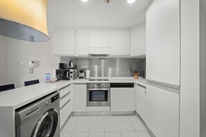A modern kitchen with white cabinetry, a built-in dishwasher, an oven, and a coffee maker. - Elegant Studio Downtown Dubai (dubai)
