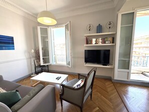 Een woonkamer met een bank, een tafel, een stoel, een televisie en een boekenkast.