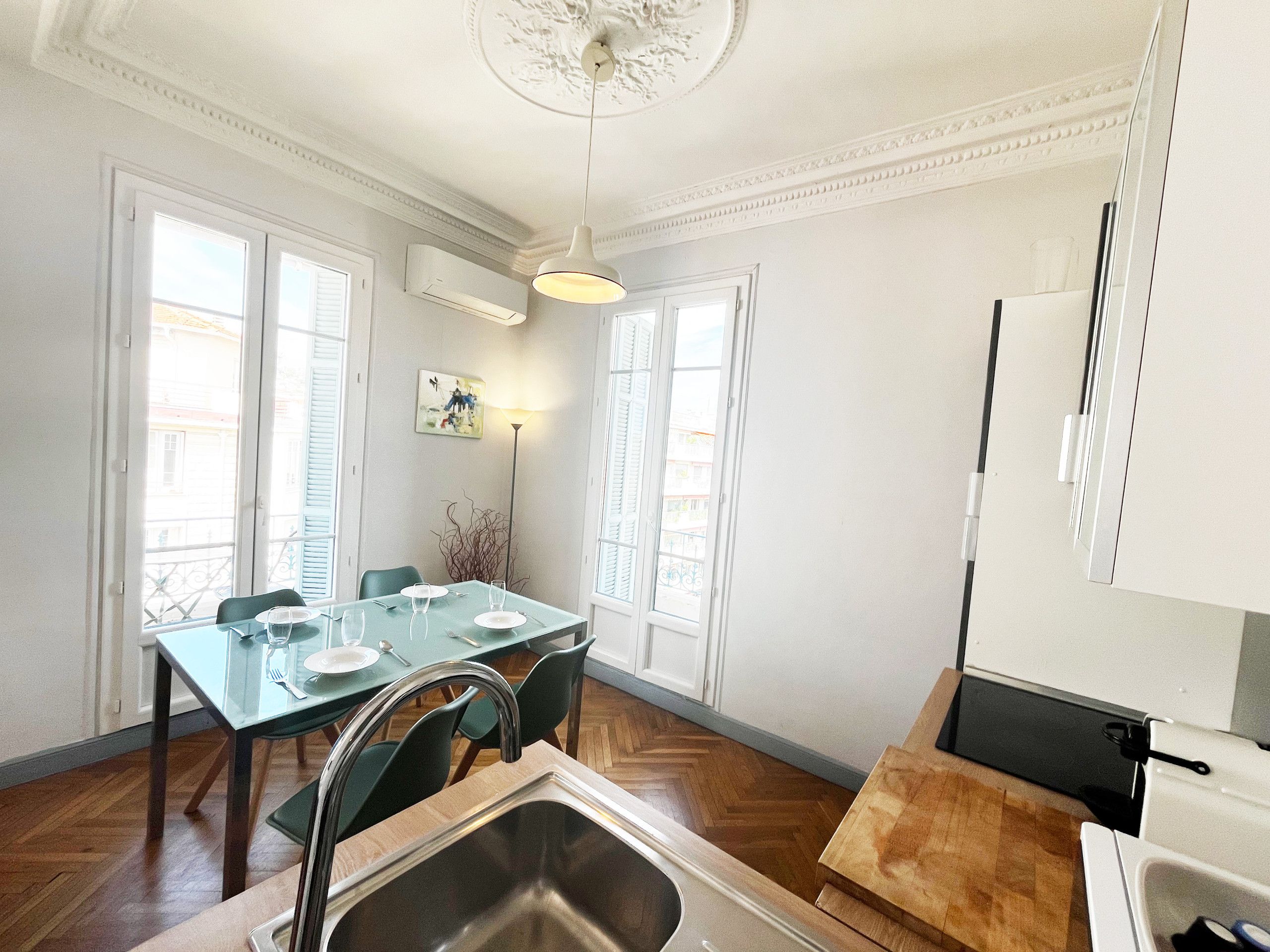Un coin repas avec une table dressée pour deux personnes, un évier et une vue sur l’extérieur grâce à de grandes fenêtres.