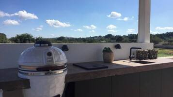 Un espace bar extérieur doté d’un barbecue intégré, d’une tablette et d’une plante en pot.