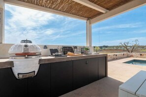 An outdoor kitchen with a built-in grill, a small table, and a view of the surrounding landscape. - *VillaMONiKA | Luxury Trulli & Pool by TrulloVista (Martina Franca)
