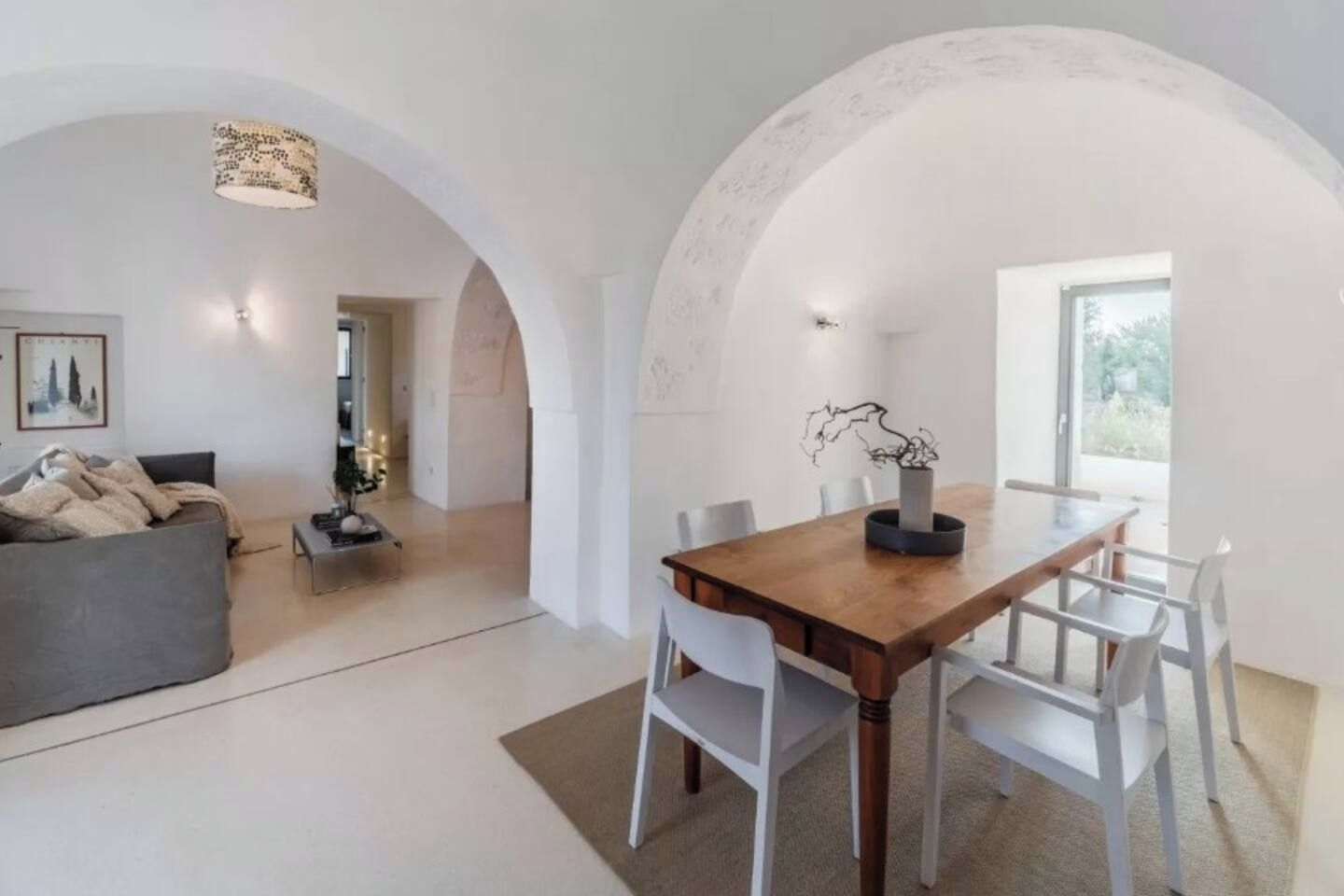Decoração moderna com sala de jantar, mesa de madeira e cadeiras brancas, sofá cinza e luminária pendente.