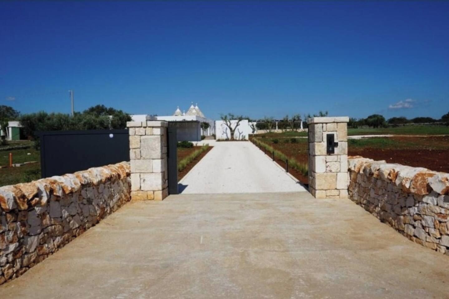 Un chemin menant à un bâtiment à la façade blanche et doté d’un mur en pierre sur un de ses côtés.