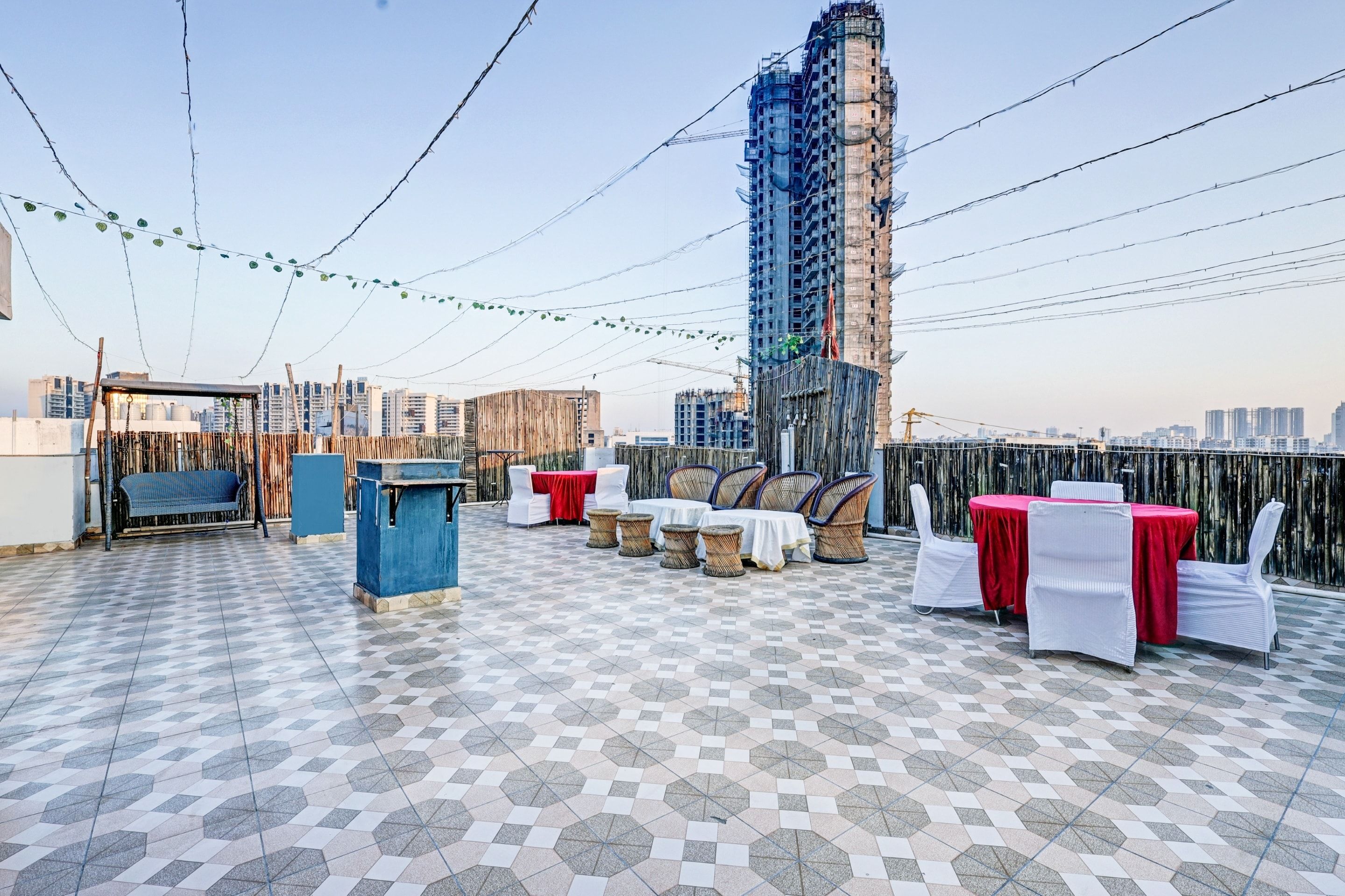 A rooftop terrace with a patterned floor, outdoor seating, and a view of a tall building under construction.